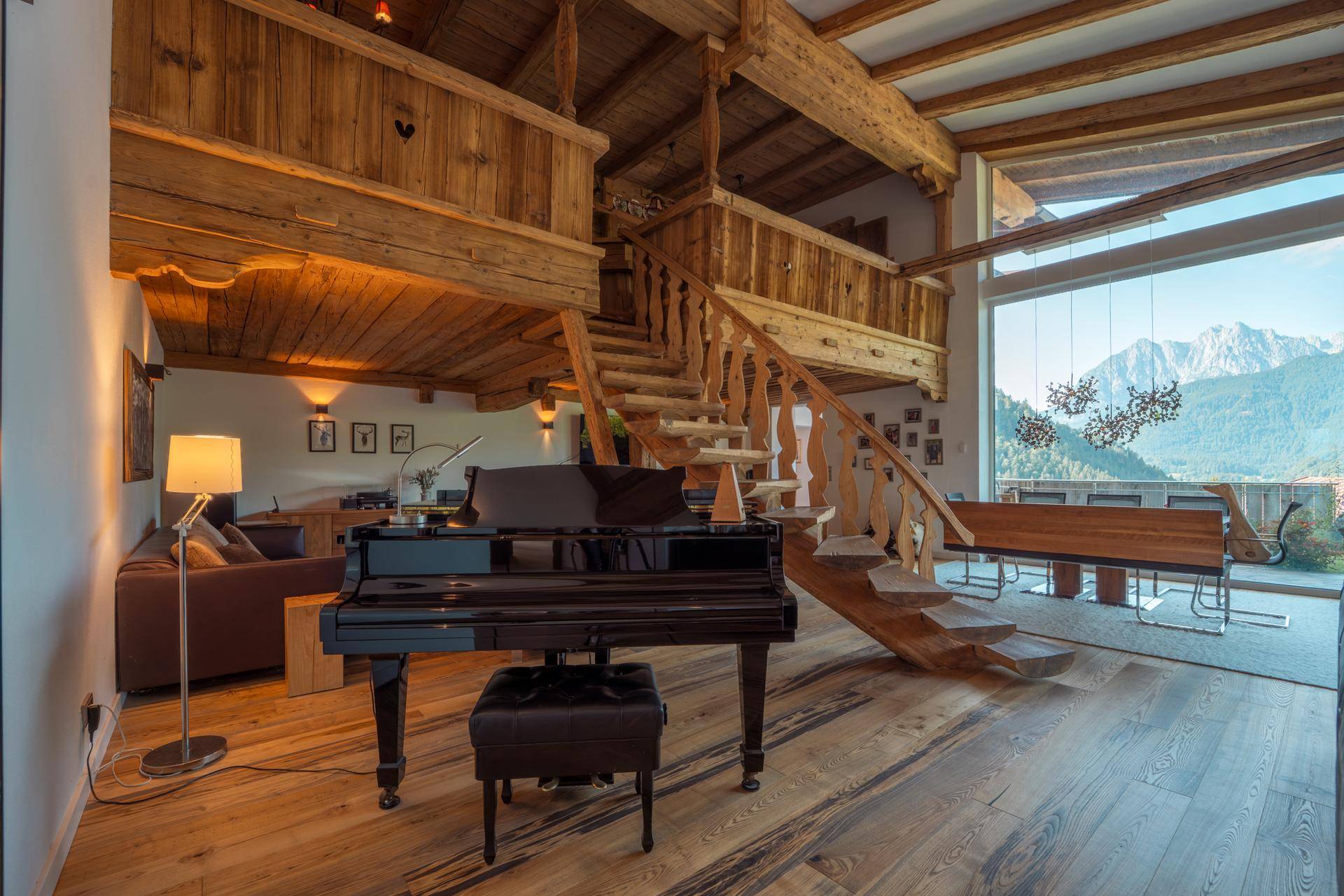 Geräumiger Wohnbereich mit Flügel, Holztreppe und Blick auf die umliegende Berglandschaft.