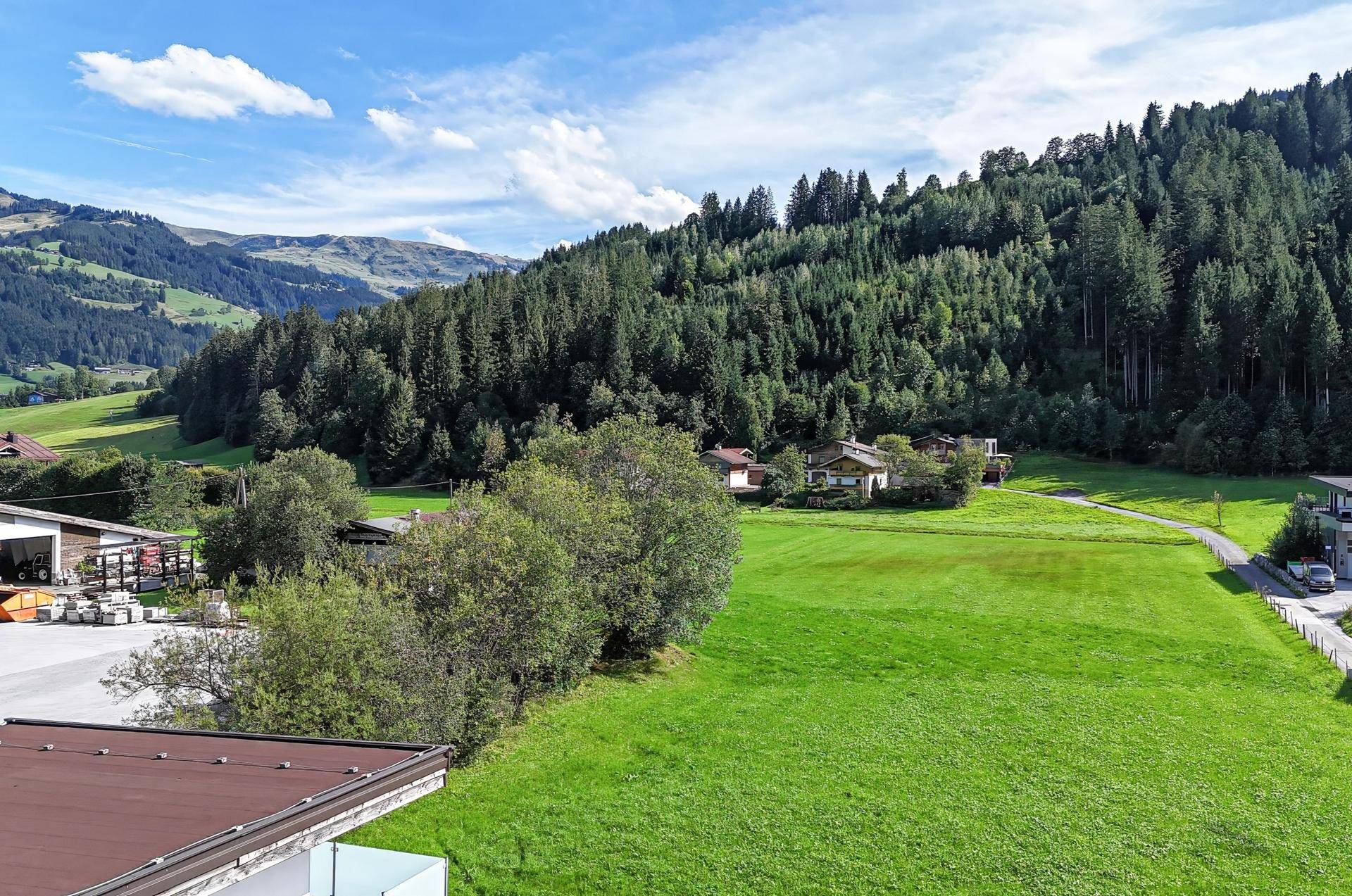 Weitläufige grüne Wiesen und bewaldete Berge unter blauem Himmel, umgeben von ländlicher Idylle.