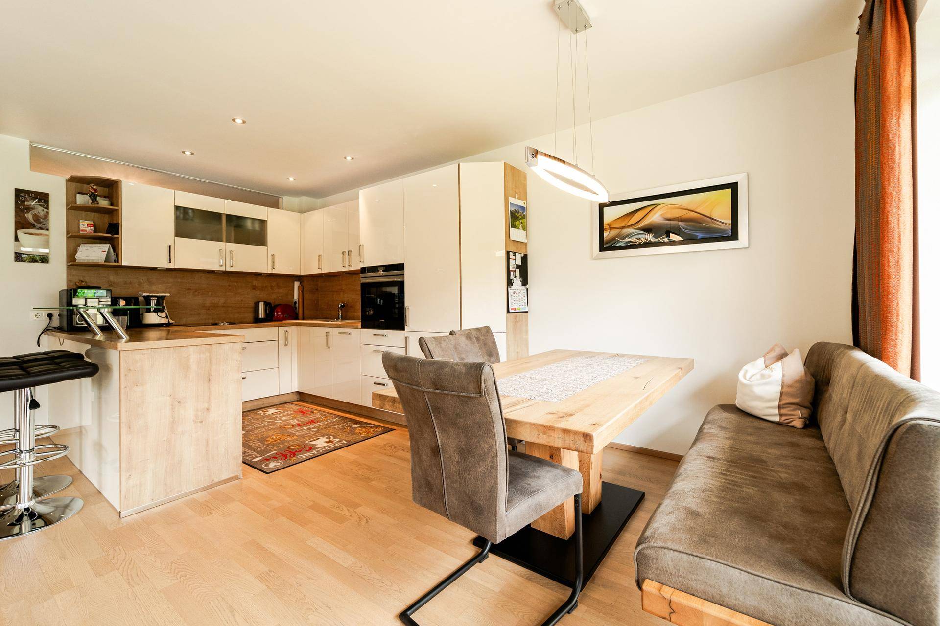 Moderne Wohnküche mit hellem Holz und weißen Hochglanzfronten, inklusive Essbereich.