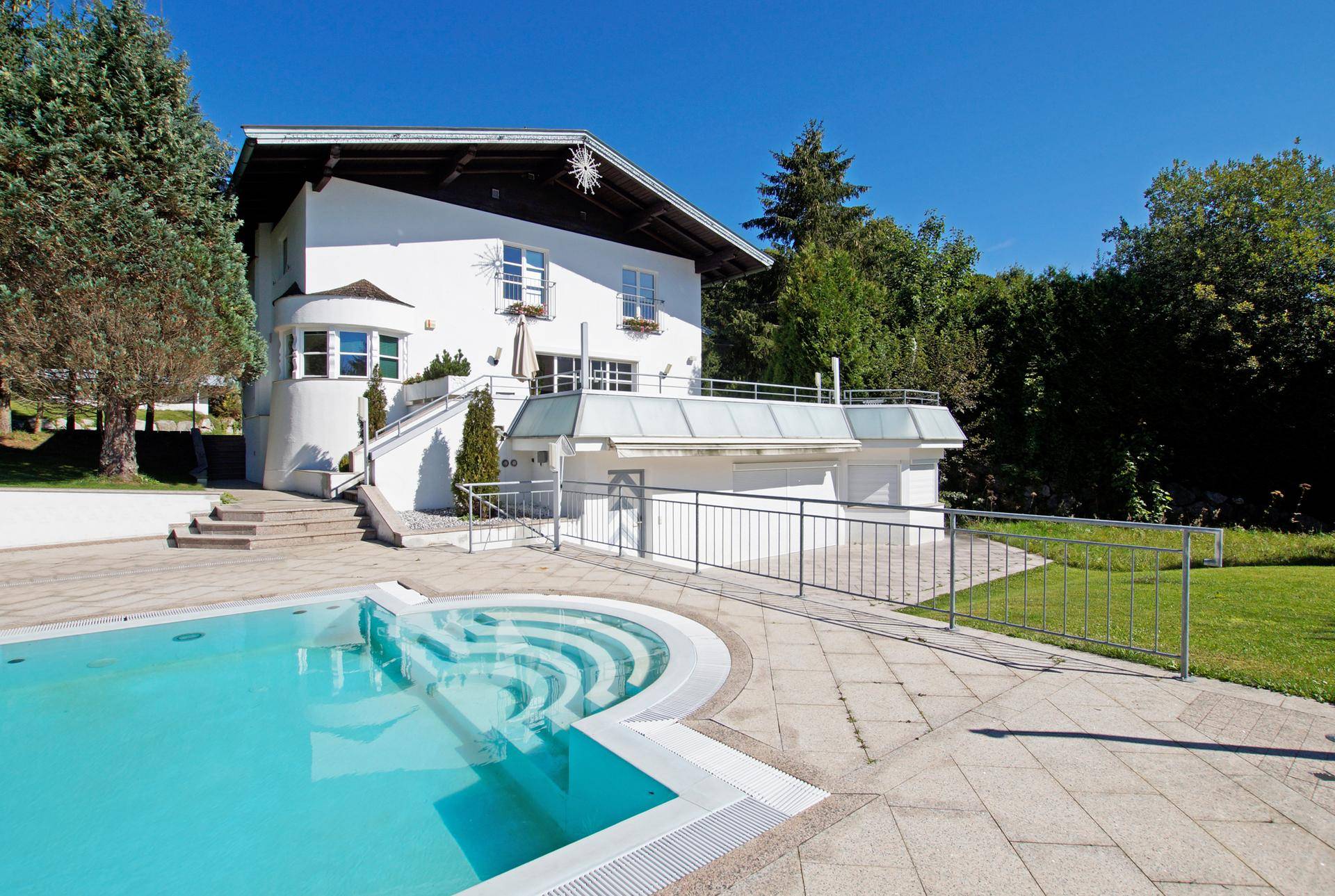 Außenansicht des weißen Hauses mit einem einladenden Poolbereich und Treppen zum Eingang.