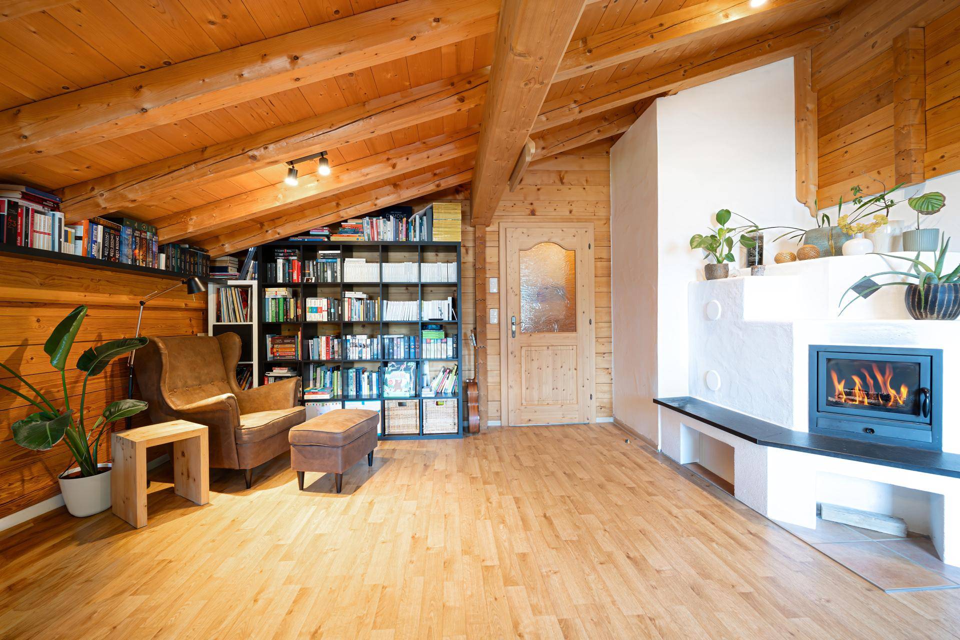 Rustikales Wohnzimmer mit Holzbalkendecke, Kamin und umfangreicher Bücherwand für gemütliche Abende.