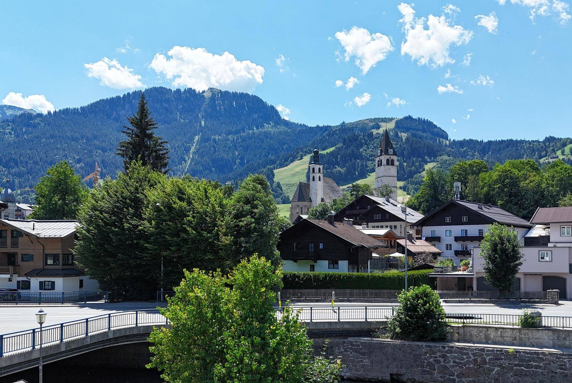 Idyllisches Dorfbild mit traditionellen Häusern, Kirche und grünen Bergen im Hintergrund.