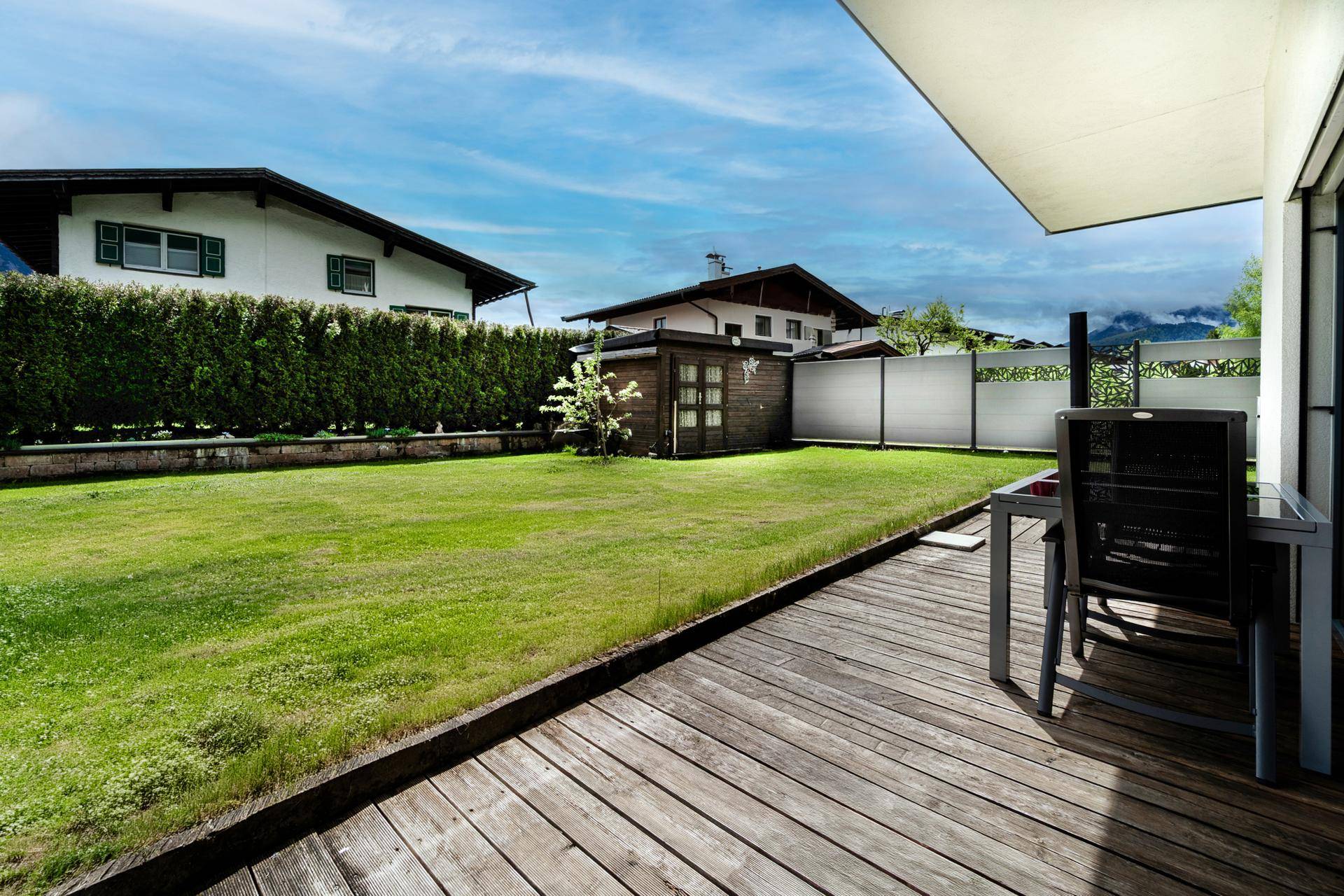 Großer, gepflegter Garten mit Rasenfläche, Gartenhaus und angrenzender Holzterrasse.