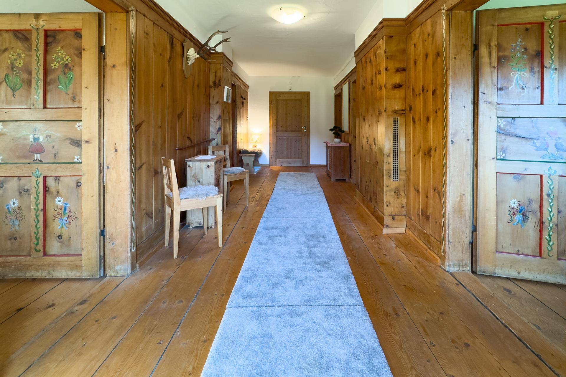 Langer Flur mit Holztäfelung, traditionellen Schränken und einem Hirschgeweih als Dekoration.