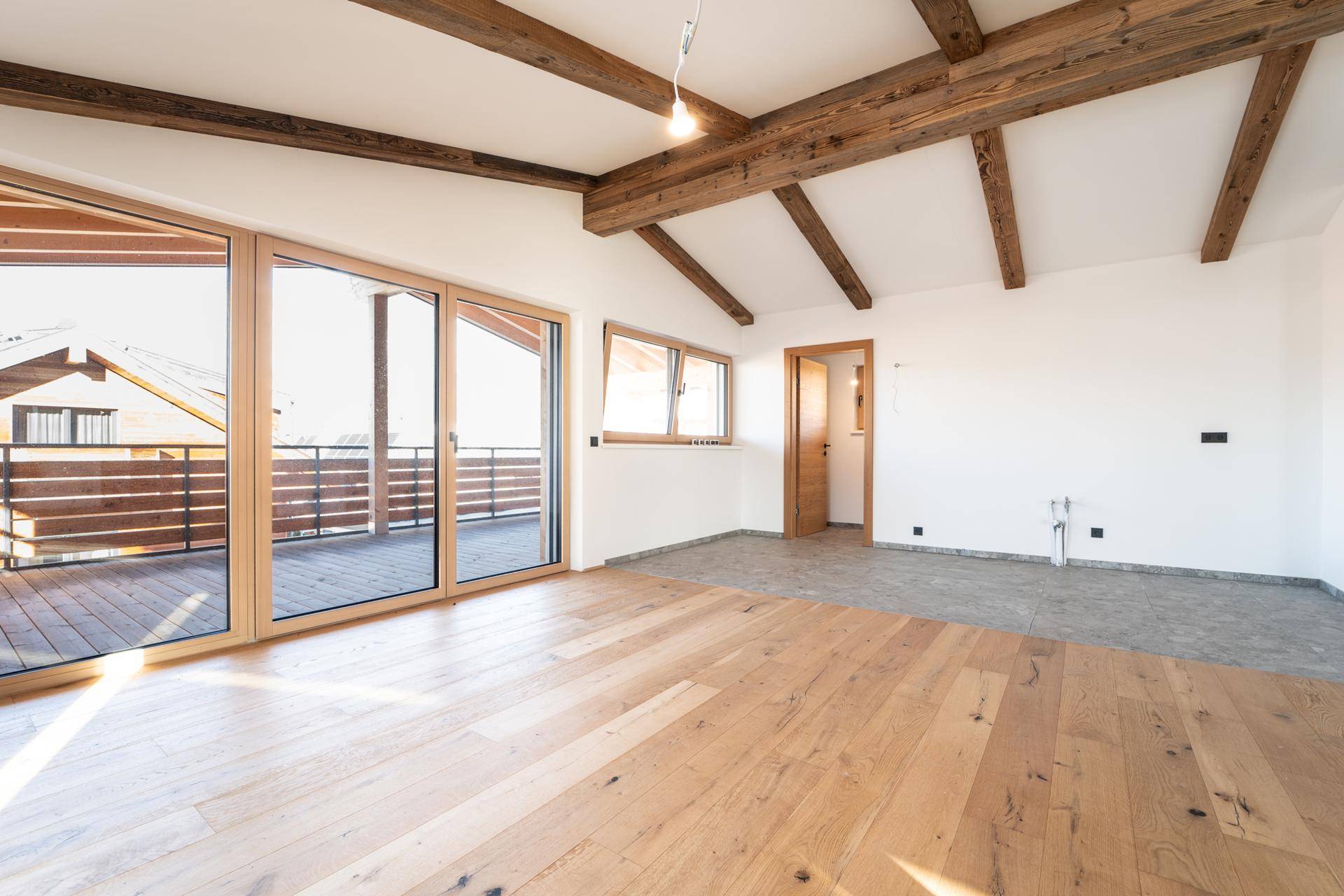 Heller Wohnbereich mit Holzbalken, großen Fenstern und Zugang zu einem sonnigen Balkon.