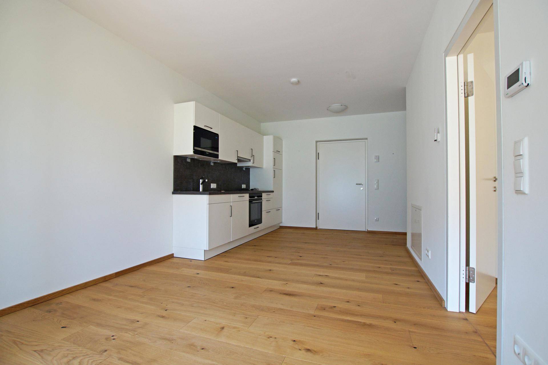 Heller Wohnbereich mit integrierter Küchenzeile, Holzboden und weiß gestrichenen Wänden.