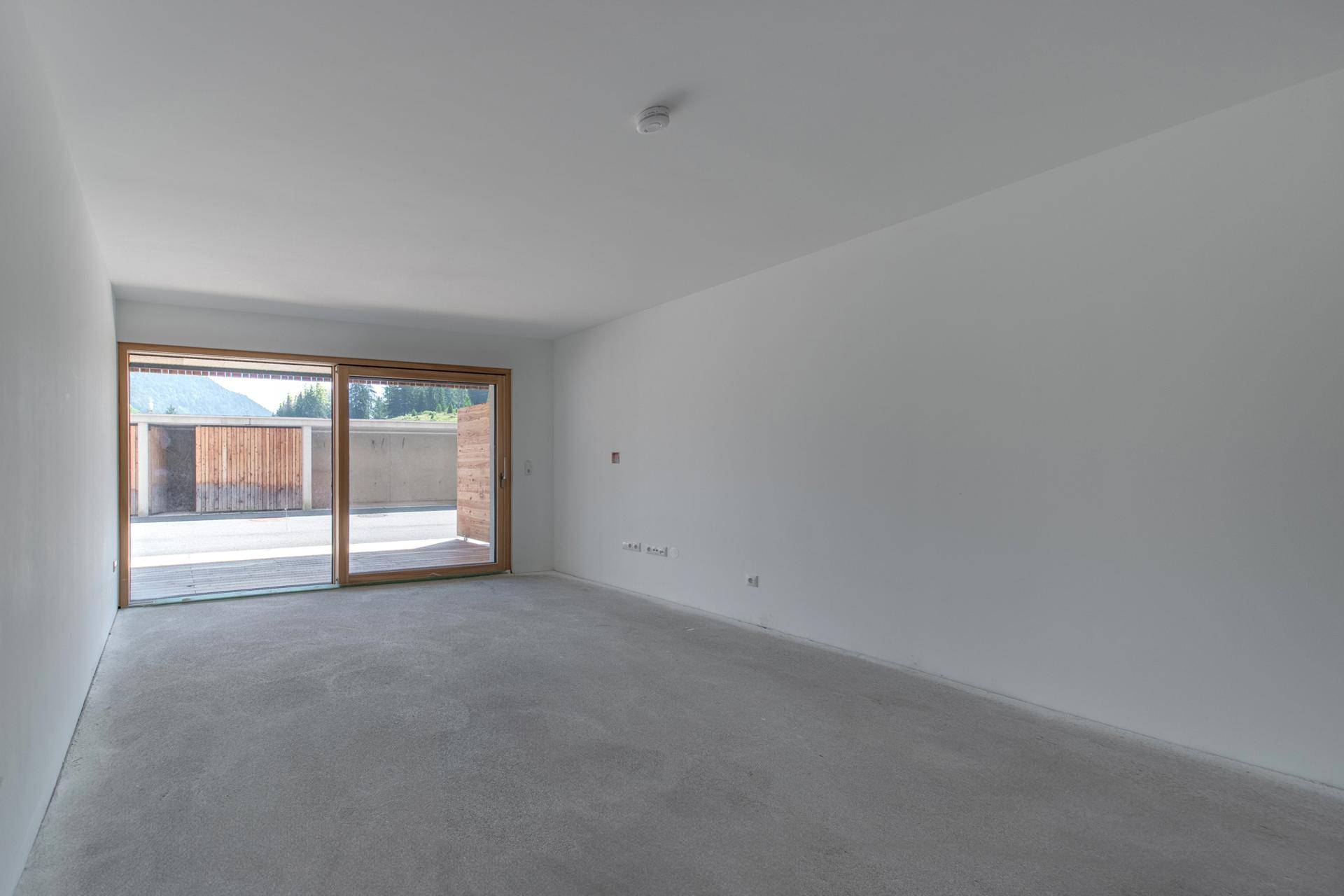 Heller, leerer Raum mit großen Schiebetüren, die Zugang zu einem Außenbereich bieten.