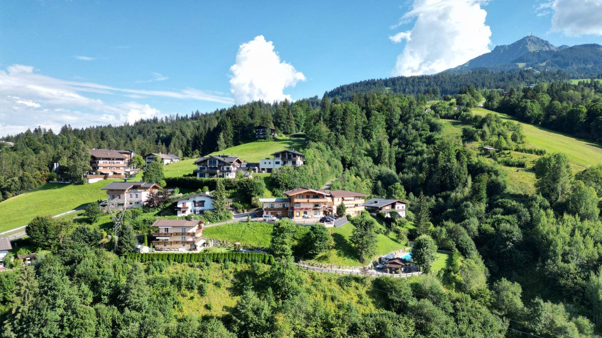 Weitläufige Luftaufnahme einer Siedlung am grünen Berghang mit vielen Häusern und Bergblick.