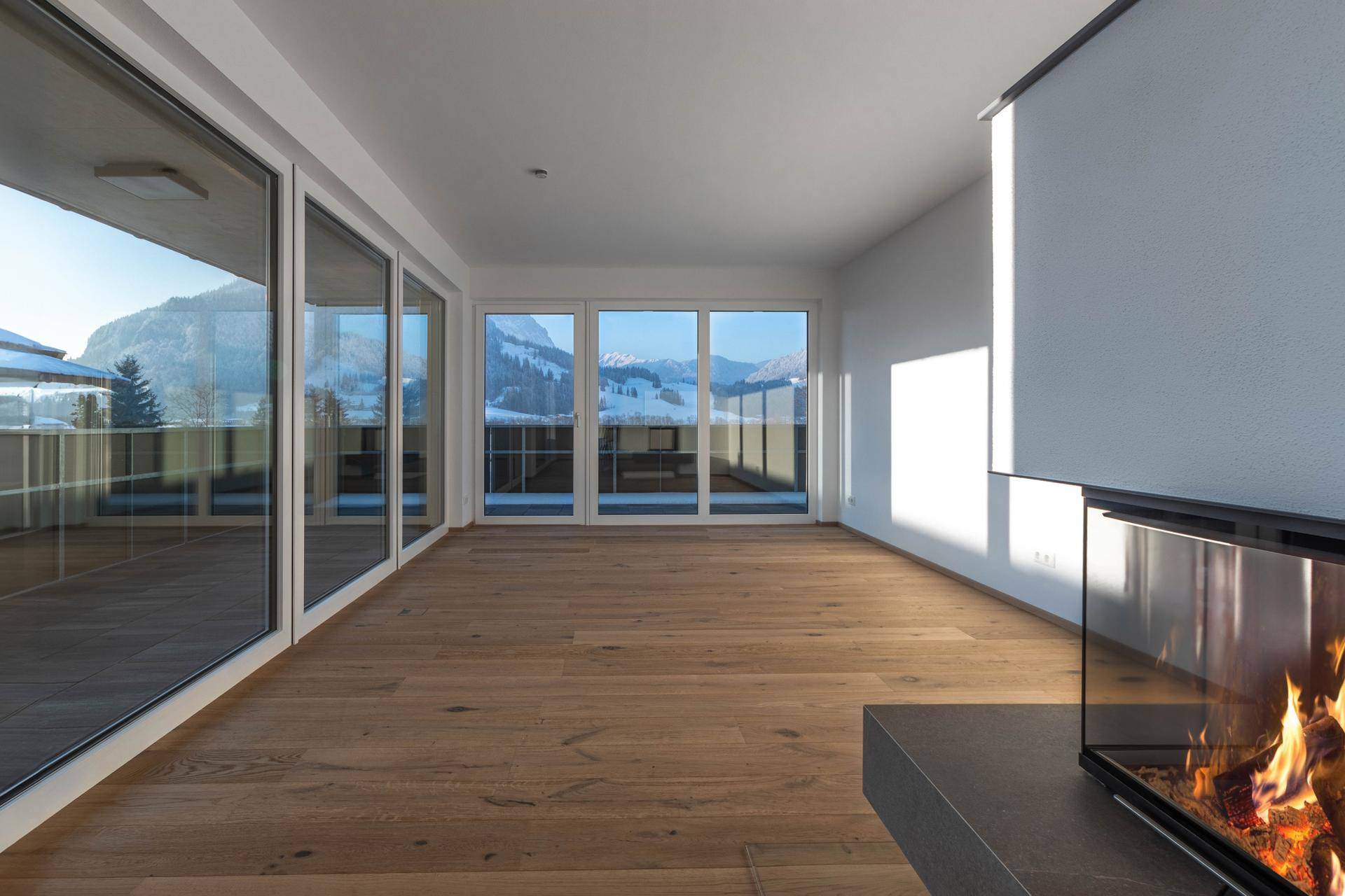 Lichtdurchfluteter Wohnbereich mit Holzboden, Kamin und Panoramafenstern mit Bergblick.