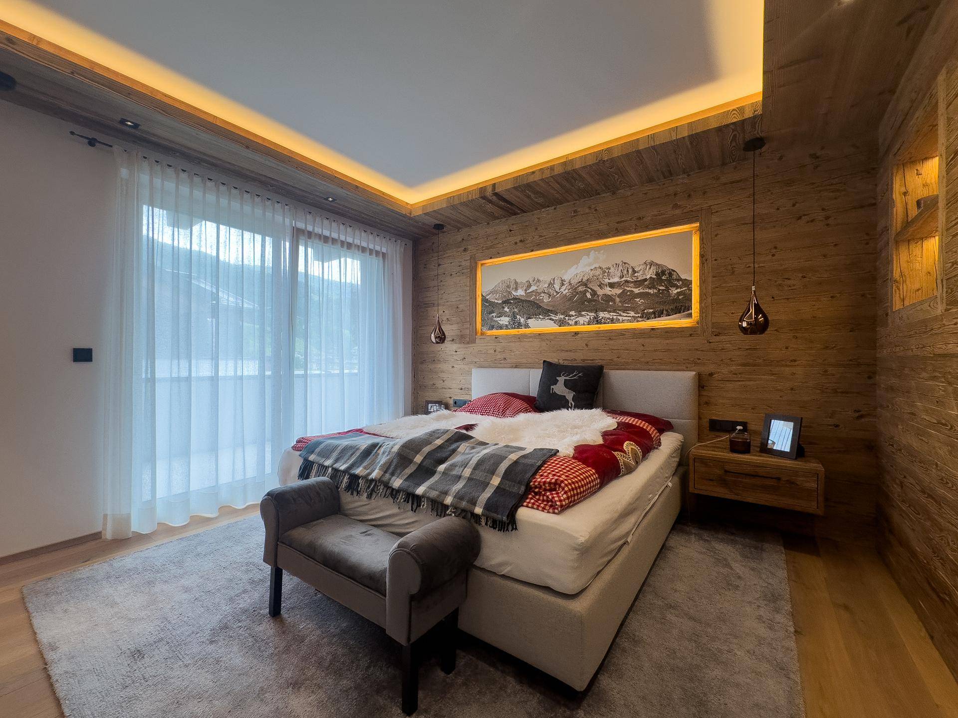 Schlafzimmer im alpinen Stil mit Holzwänden, indirekter Beleuchtung und Zugang zu einem Balkon.
