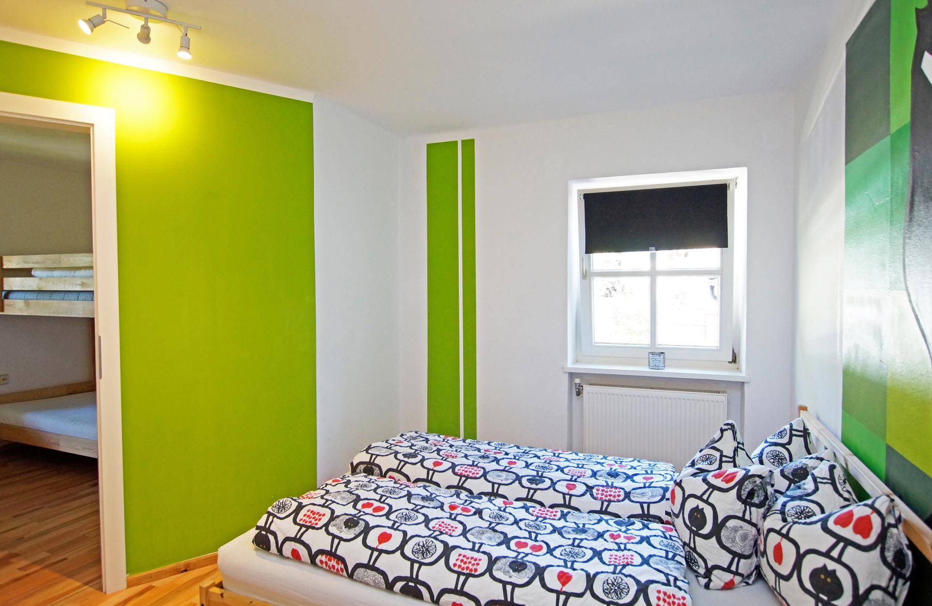Helles Schlafzimmer mit Doppelbett, Holzboden und einer auffälligen grünen Akzentwand.