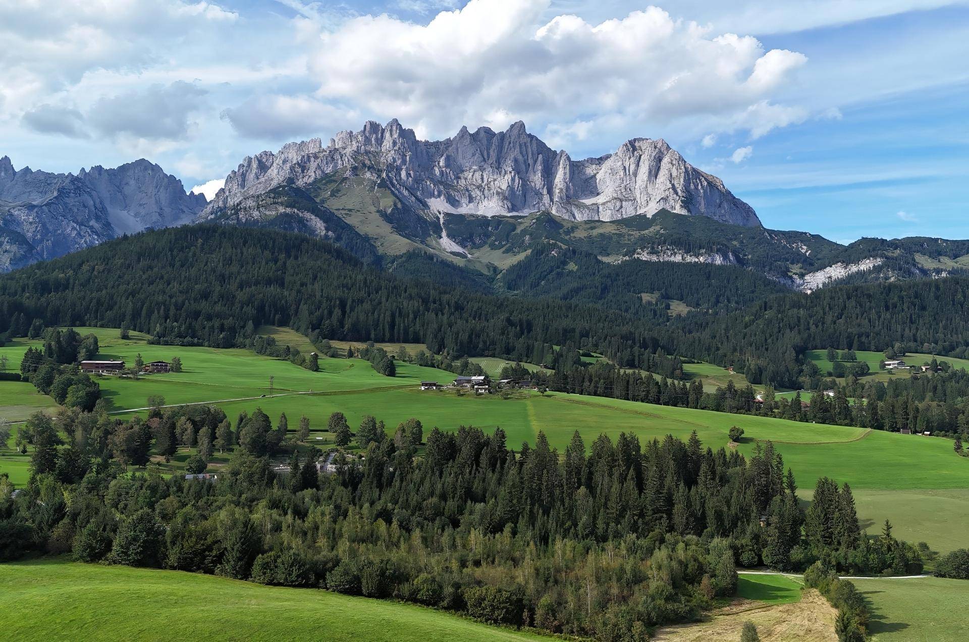 Panoramablick auf eine weite grüne Landschaft mit Wäldern, Hügeln und majestätischen Bergen.