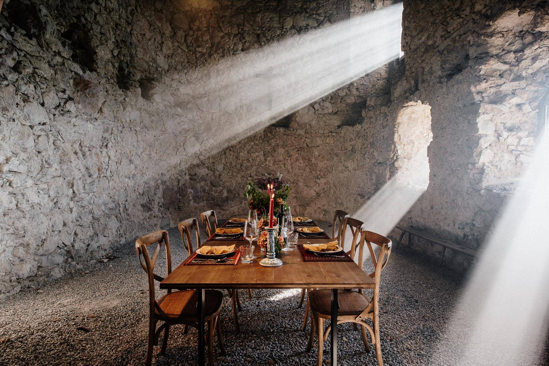 Rustikaler Essbereich mit Steinfassade, Holztisch und dramatischen Lichtstrahlen.