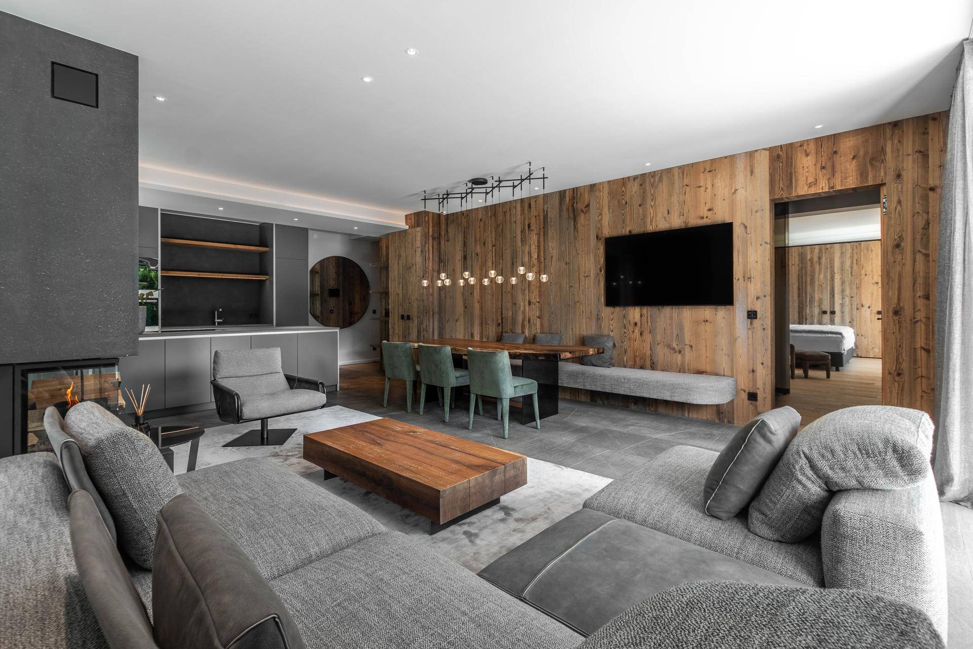 Moderner Wohn- und Essbereich mit Holzwand, Kamin und offener Küche, die zum Schlafzimmer führt.
