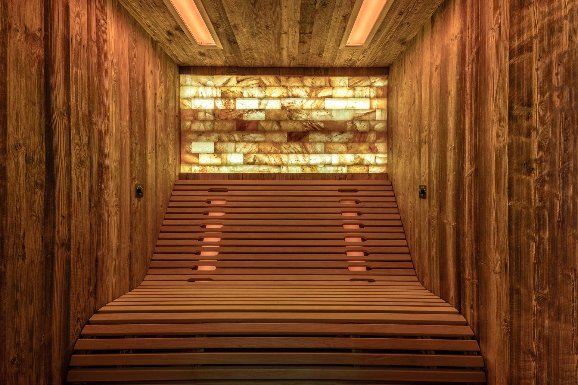 Innenansicht einer modernen Sauna mit Holzverkleidung, bequemen Bänken und einer beleuchteten Salzsteinwand.