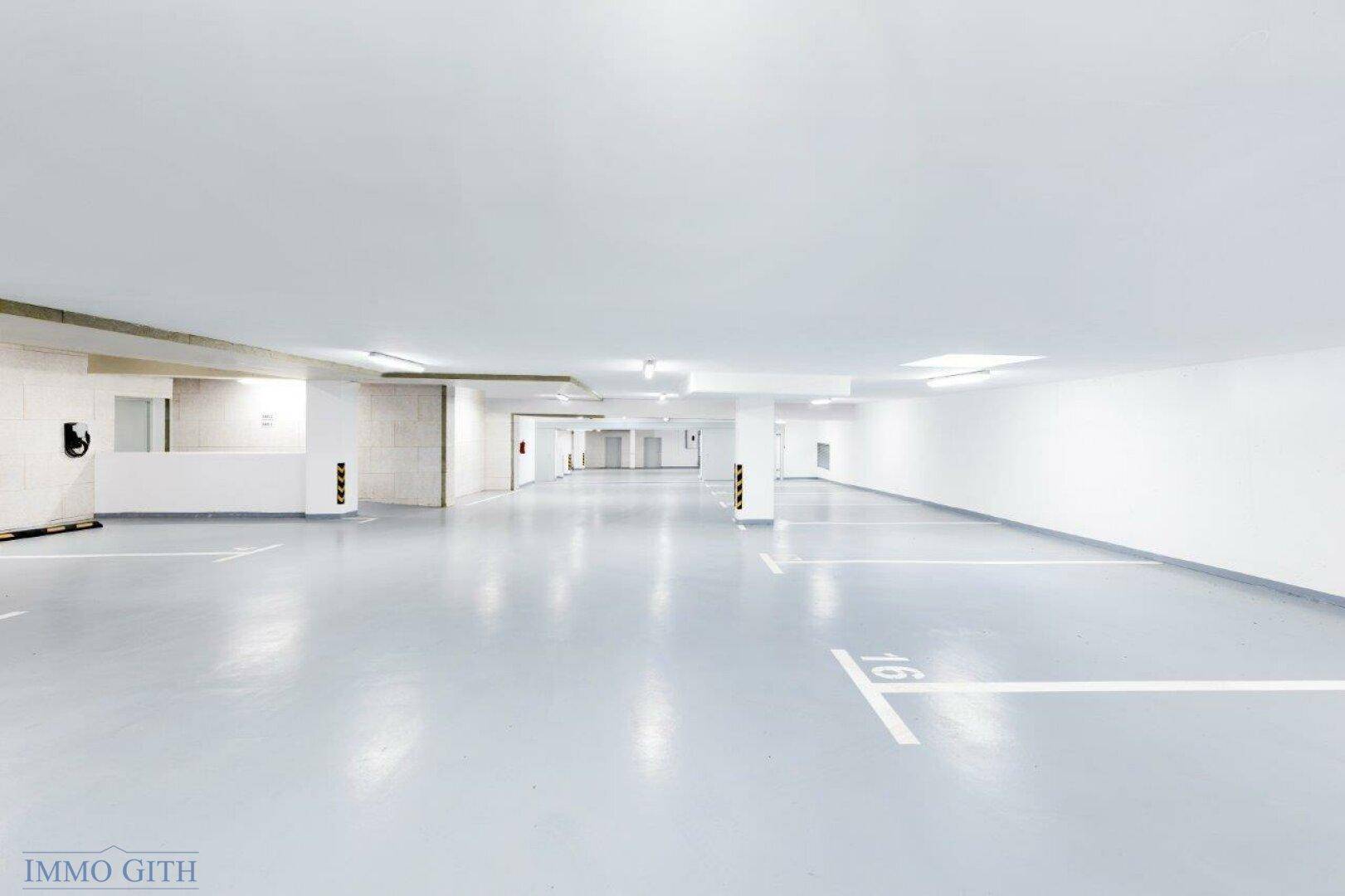 Helle und geräumige Tiefgarage mit markierten Stellplätzen und einer Ladestation für Elektrofahrzeuge.