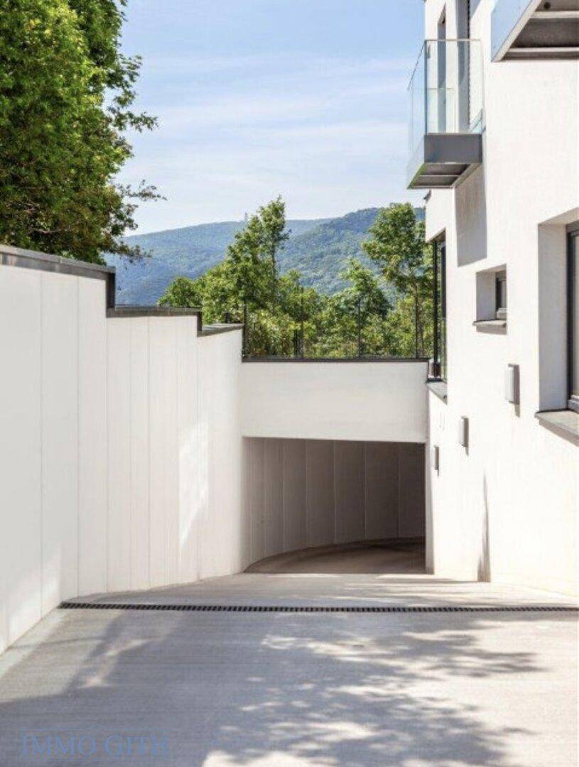 Moderner Gebäudeeingang mit Zufahrt zur Tiefgarage und malerischem Bergblick im Hintergrund.