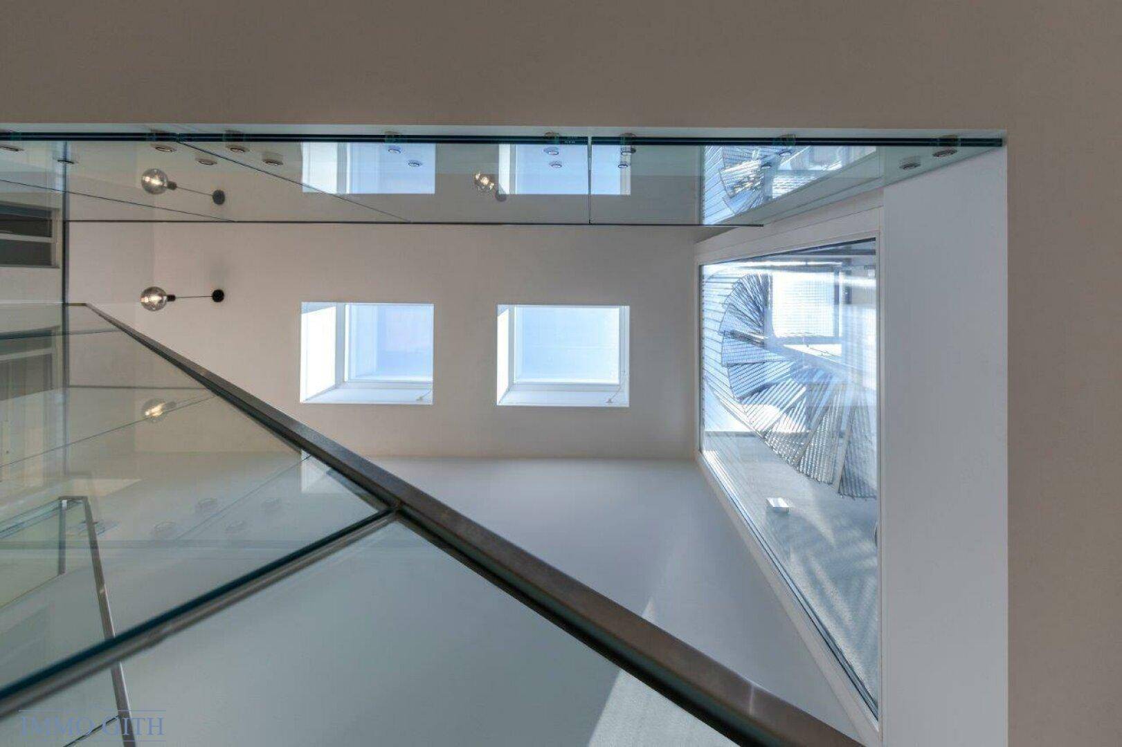 Blick nach oben im Treppenhaus mit Oberlichtern und einer Wendeltreppe im Hintergrund.
