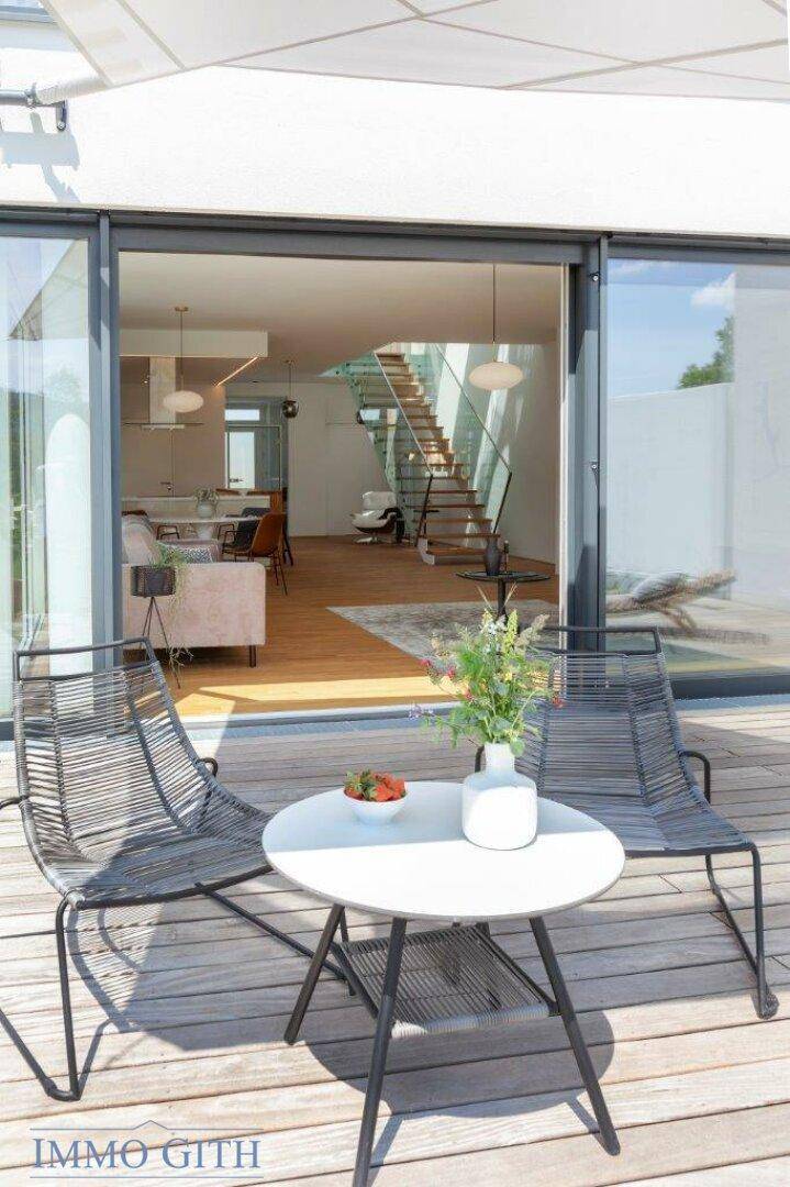 Gemütliche Terrasse mit Sitzgelegenheiten und Blick in den hellen Wohnbereich des Hauses.