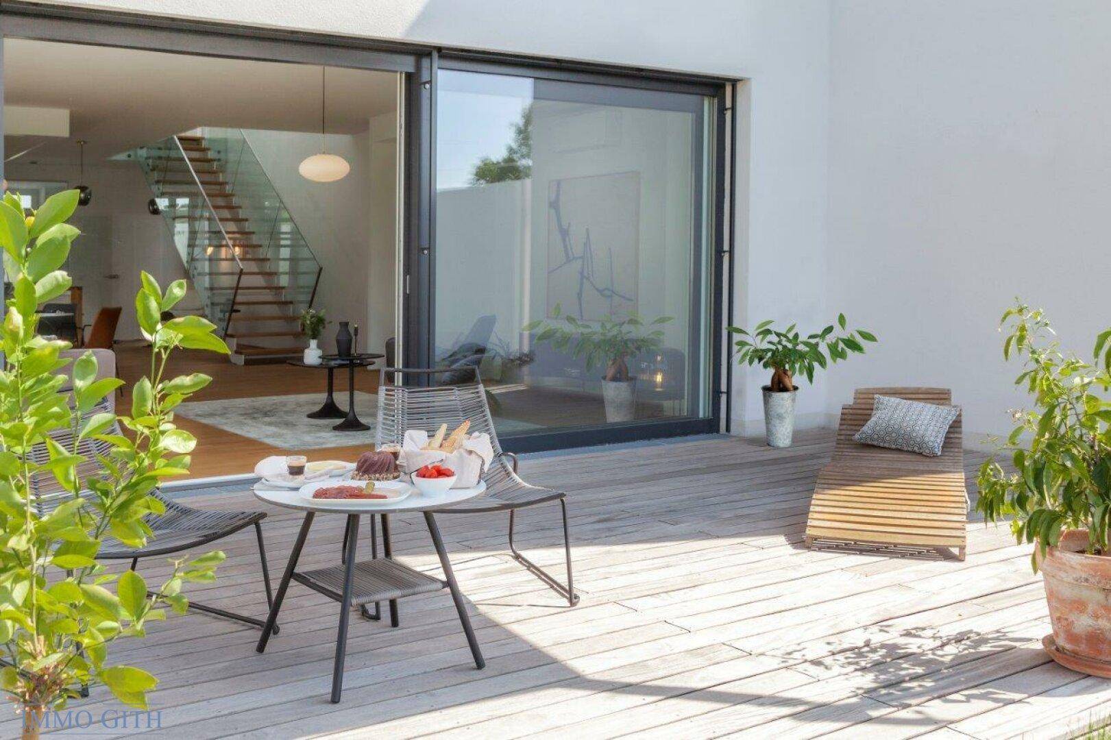 Geräumige Holzterrasse mit Sonnenliege und Blick in den modernen Wohnbereich.