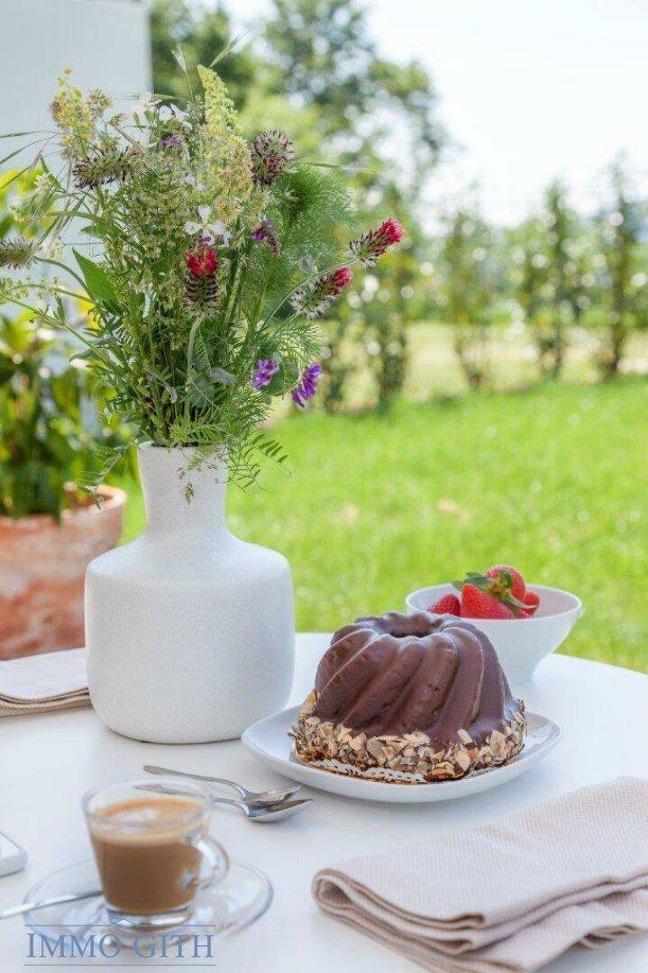 Nahaufnahme von Kuchen und Kaffee auf einem Terrassentisch mit grünem Garten im Hintergrund.