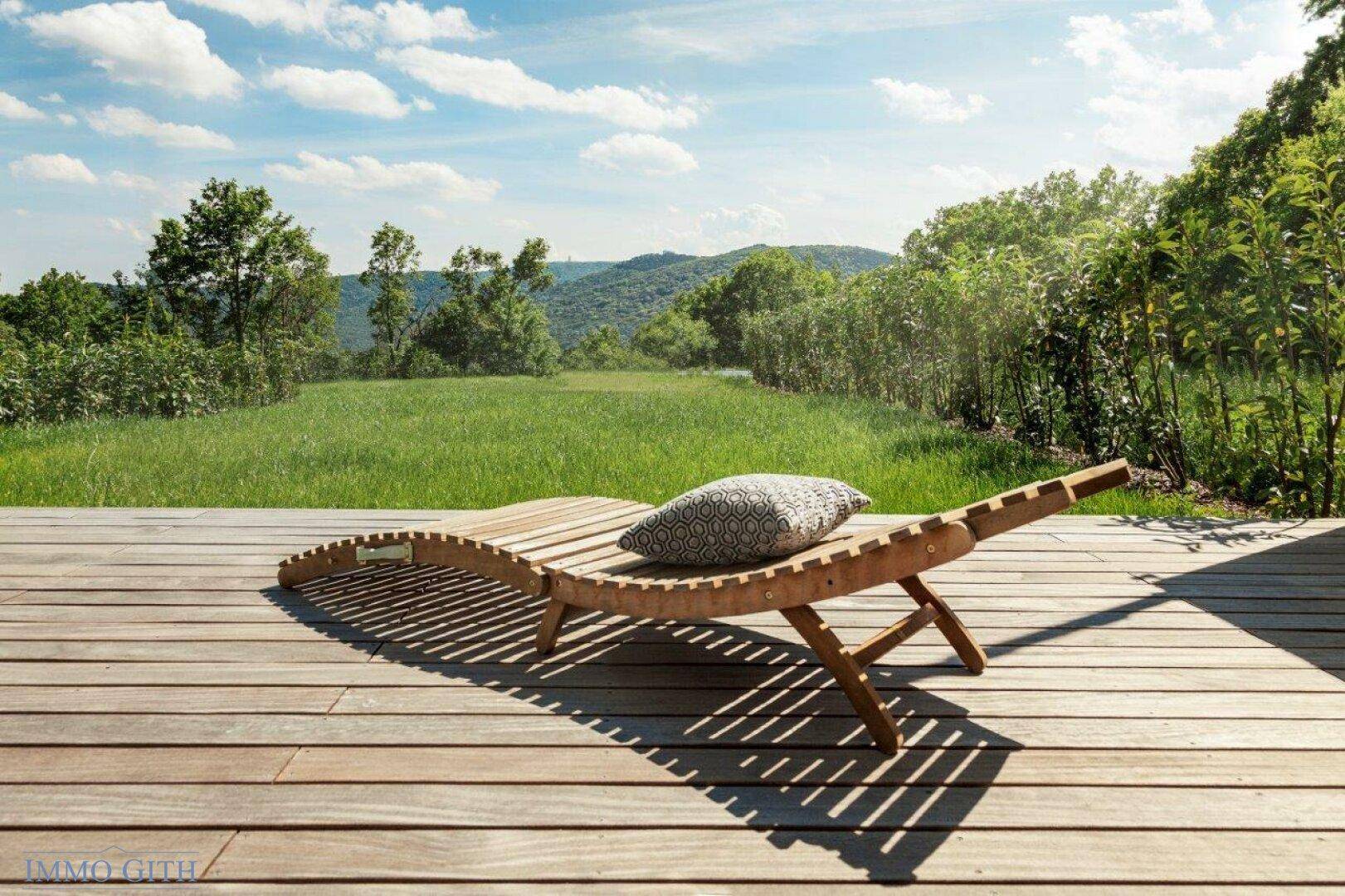 Holzliege auf der Terrasse mit weitem Blick über die grüne Landschaft und Hügel.