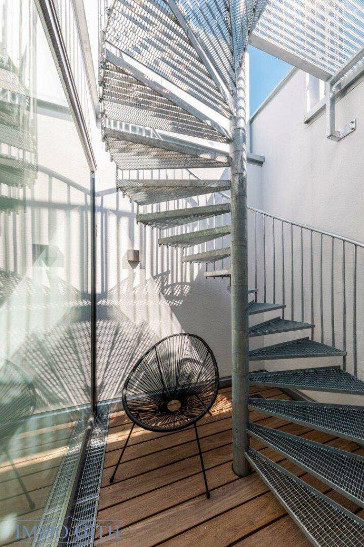 Moderne Wendeltreppe aus Metall mit Glaswänden, die zu einem oberen Bereich führt.