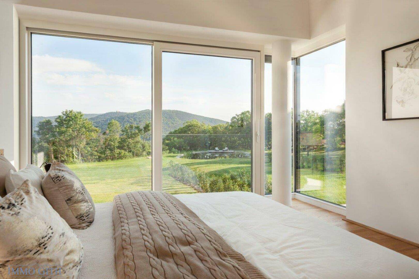 Helles Schlafzimmer mit großen Panoramafenstern und weitem Blick auf die grüne Landschaft.