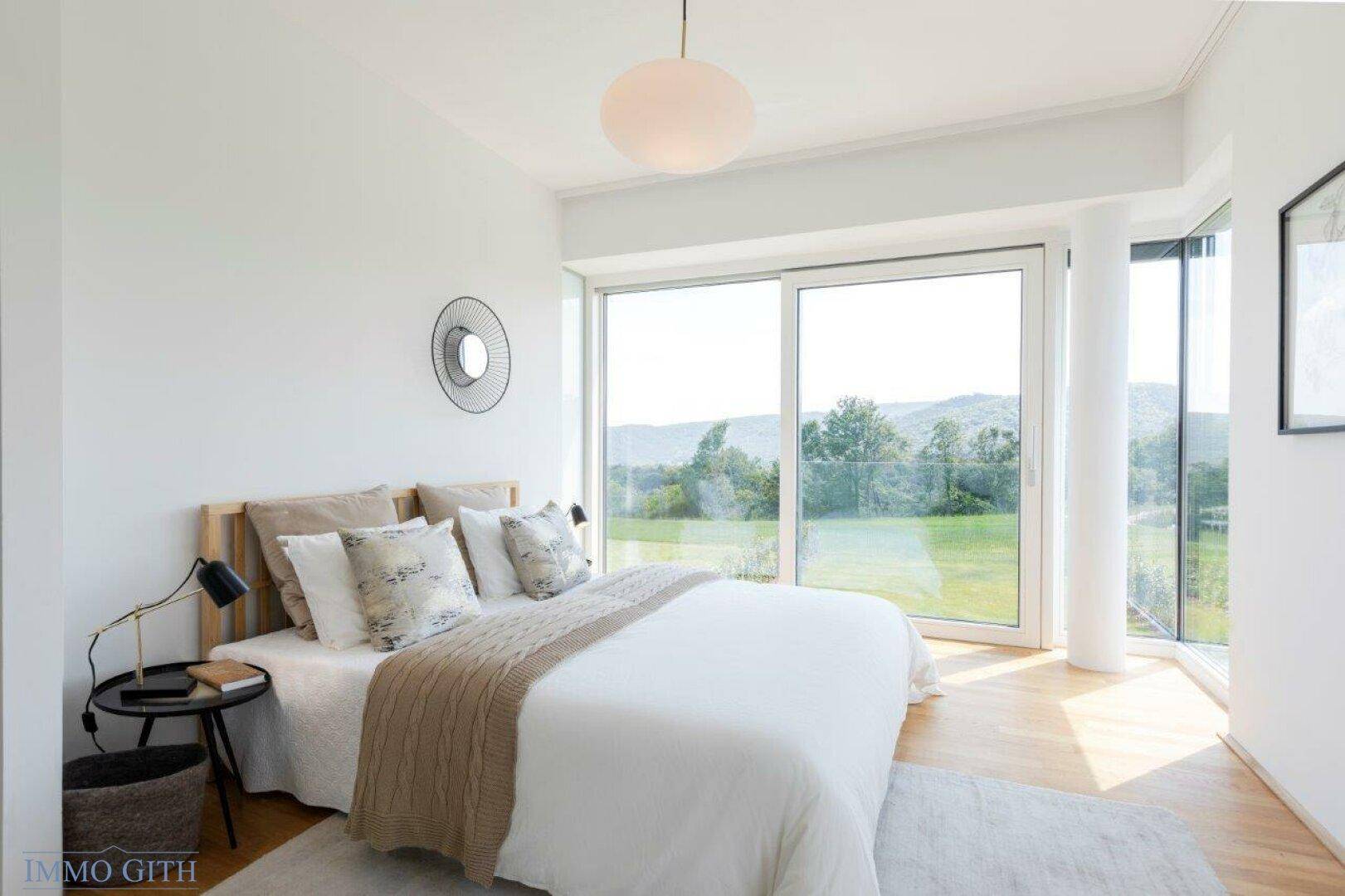 Modernes Schlafzimmer mit Doppelbett, minimalistischer Einrichtung und großen Fenstern.