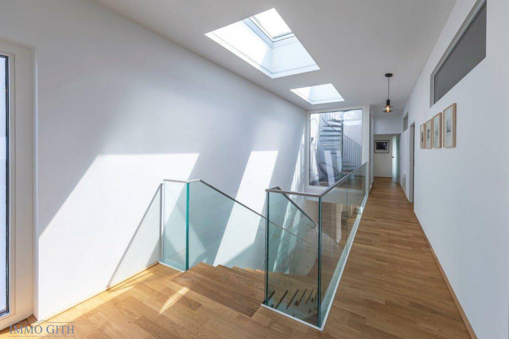 Heller Flur im Obergeschoss mit Holztreppe, Glasgeländer und Oberlichtern für viel Licht.