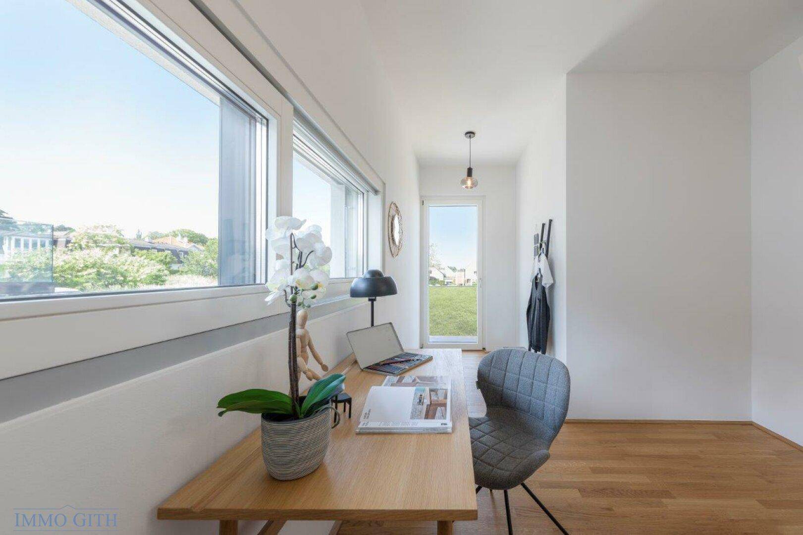 Heller Arbeitsbereich mit Holztisch, großen Fenstern und Blick ins Grüne.