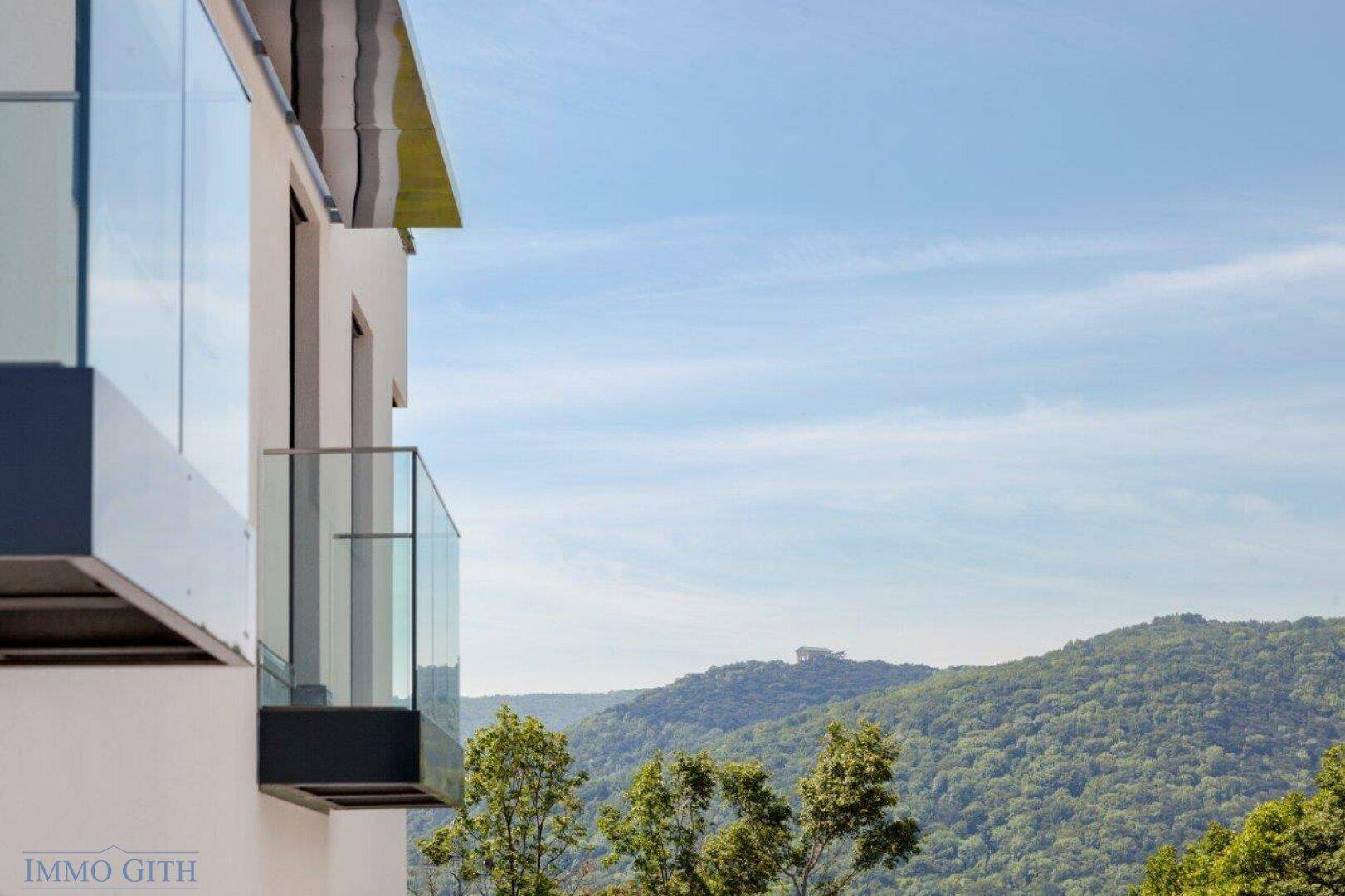 Moderner Balkon mit Glasbrüstung und weitem Blick auf die bewaldeten Hügel.