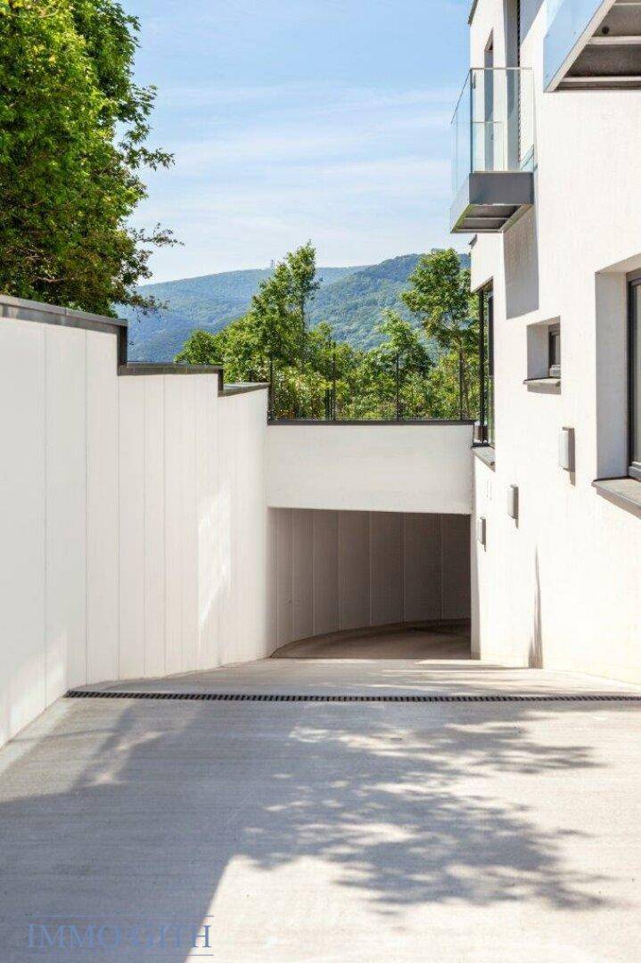 Moderne Gebäudefassade mit Zufahrt zur Tiefgarage, umgeben von grüner Landschaft.