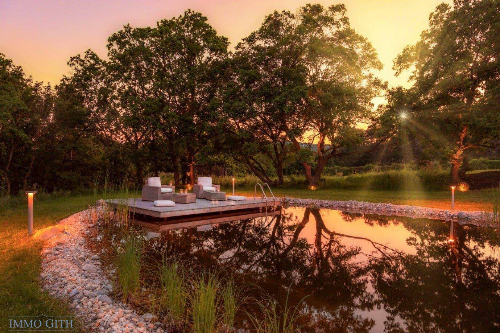 Natürlicher Schwimmteich mit Holzdeck und gemütlicher Lounge-Ecke im Garten.