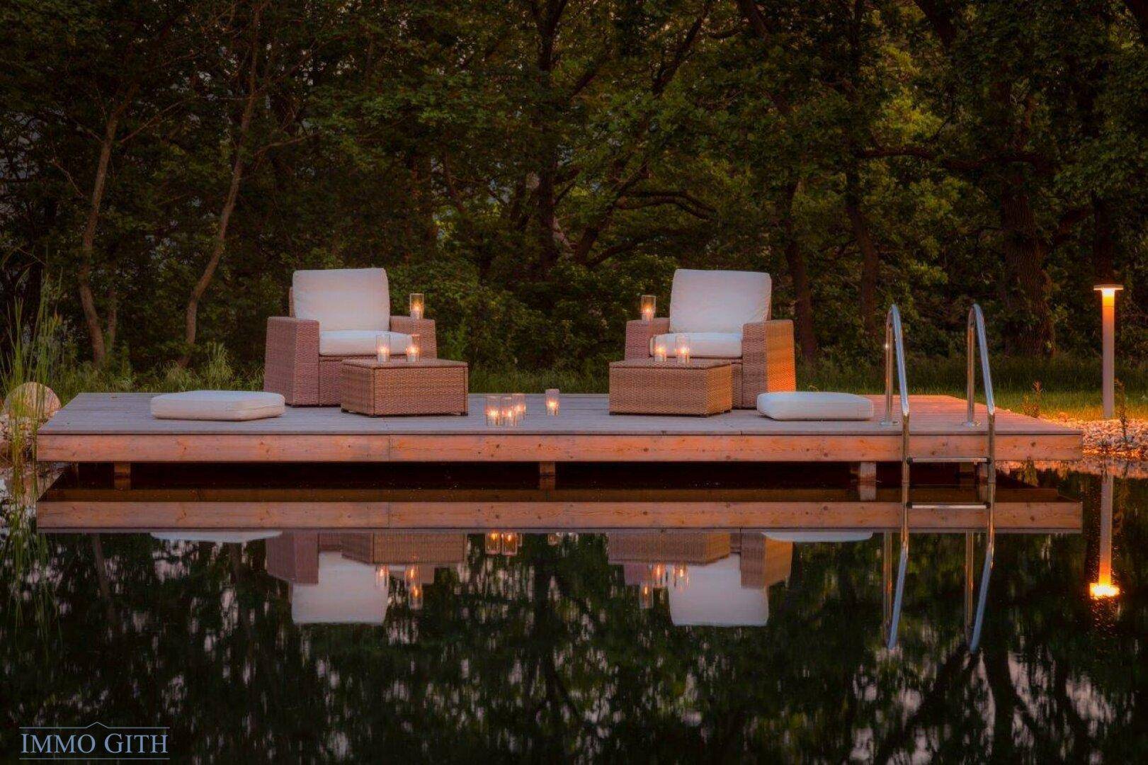 Elegantes Holzdeck am Schwimmteich mit bequemen Loungemöbeln und stimmungsvoller Beleuchtung.