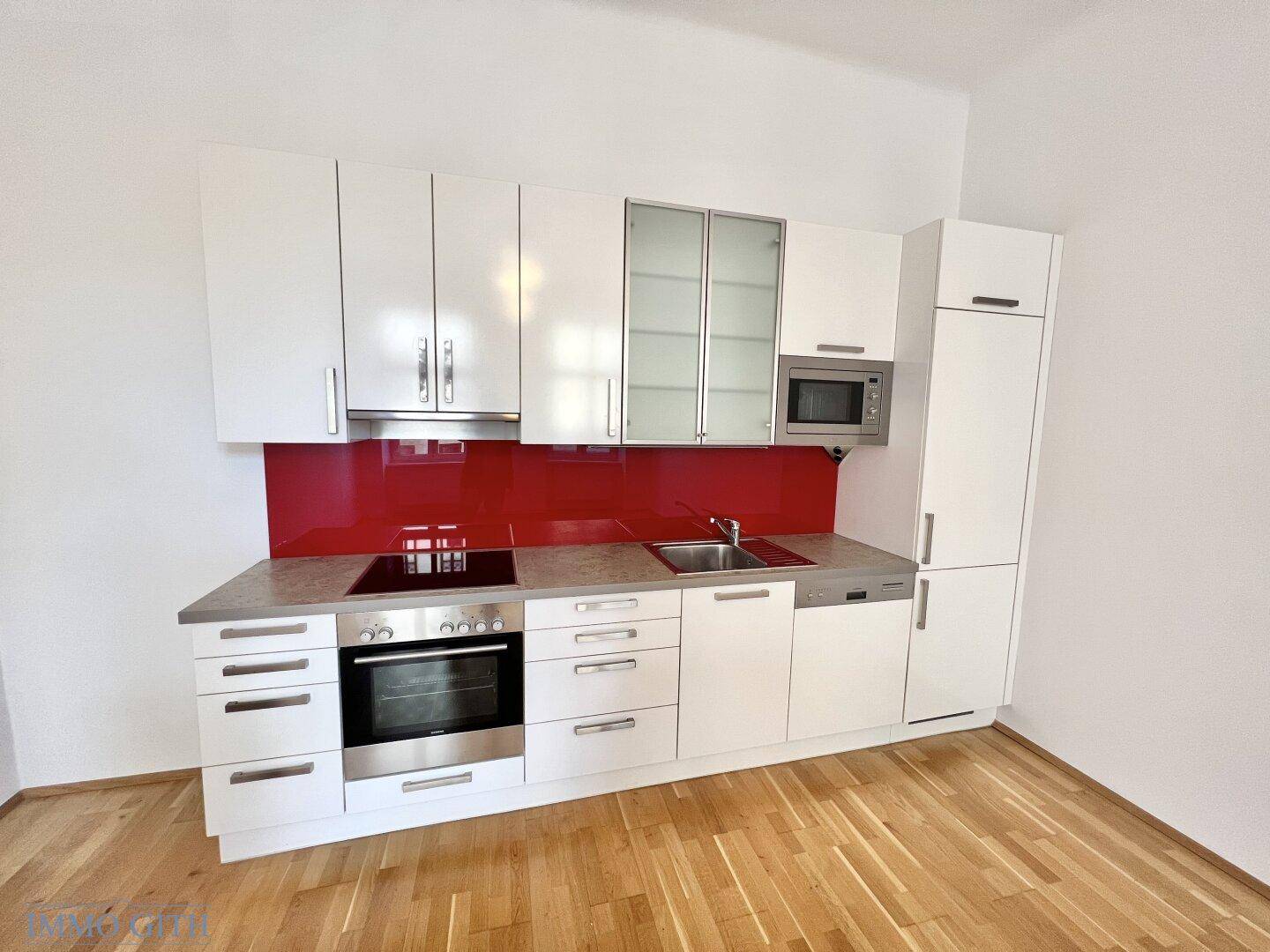 Moderne Einbauküche mit weißen Schränken, roter Rückwand und integrierten Edelstahlgeräten.