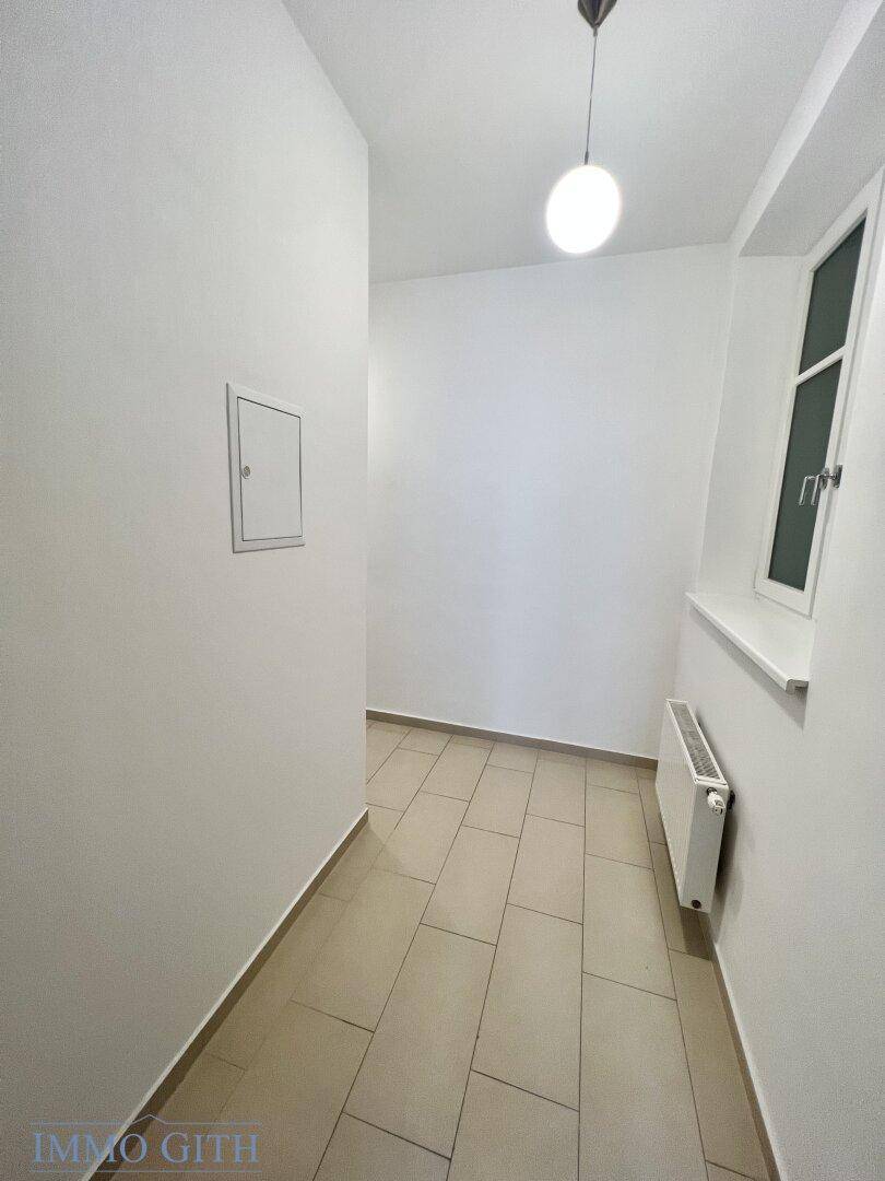 Heller Flur mit Fliesenboden und einem Fenster, das Tageslicht hereinlässt und den Raum erhellt.