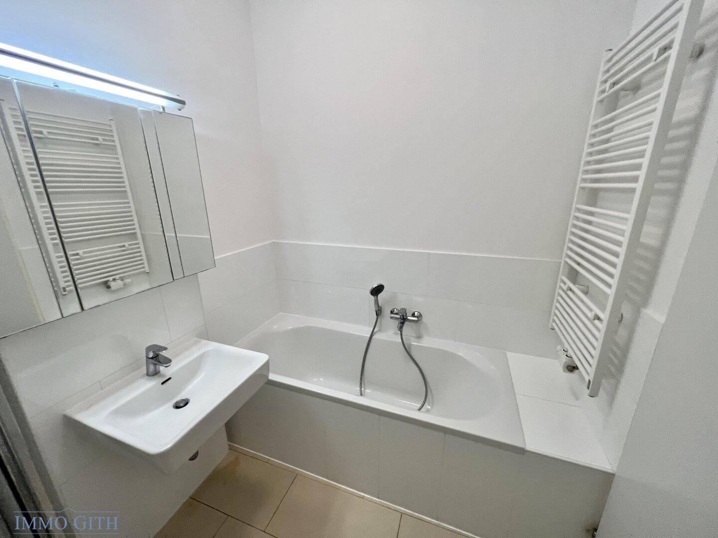 Helles Badezimmer mit Badewanne, Waschbecken und beheiztem Handtuchhalter, praktisch und komfortabel.