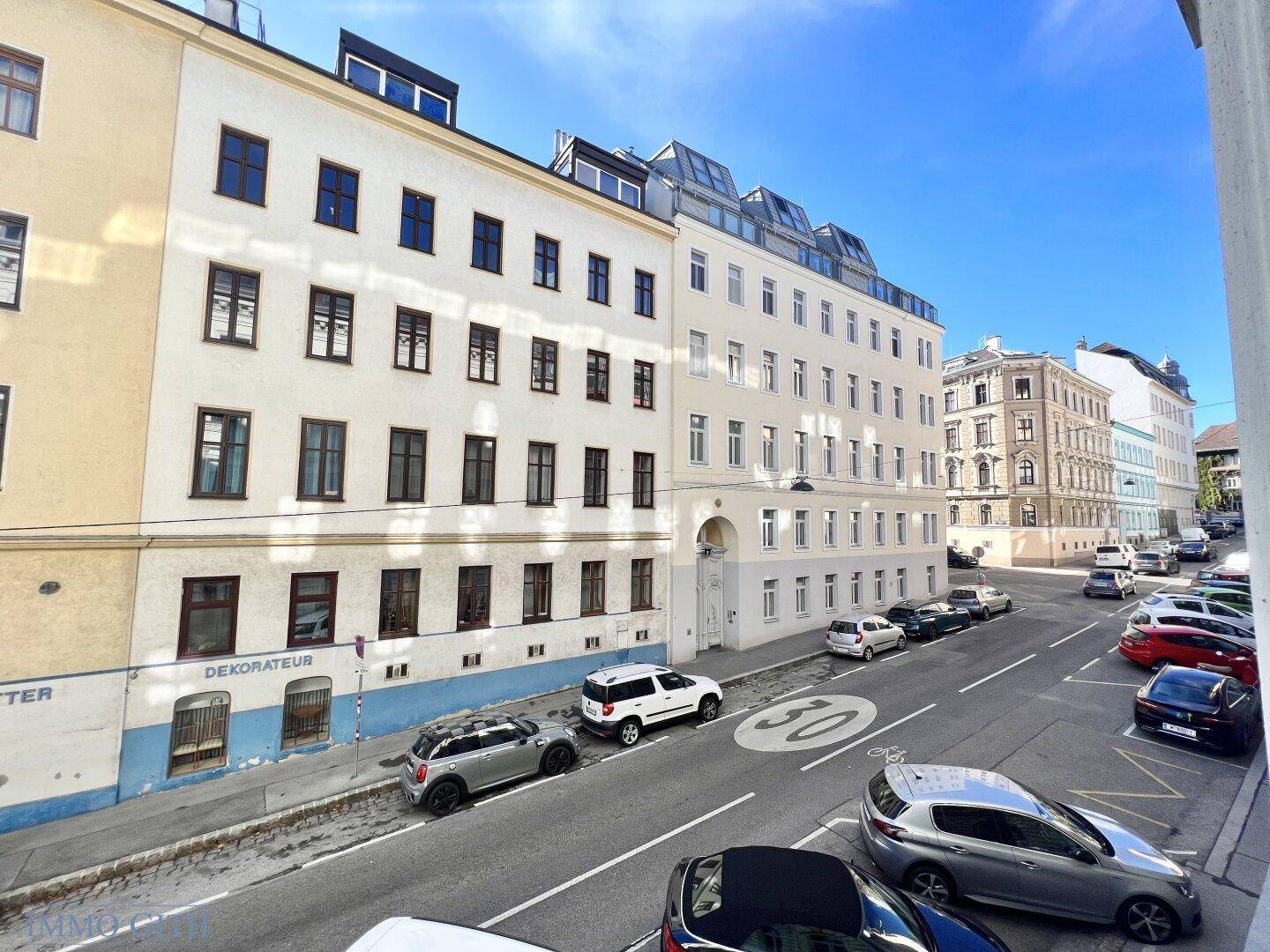 Weitblick über eine städtische Straße mit parkenden Fahrzeugen und angrenzenden Wohngebäuden.