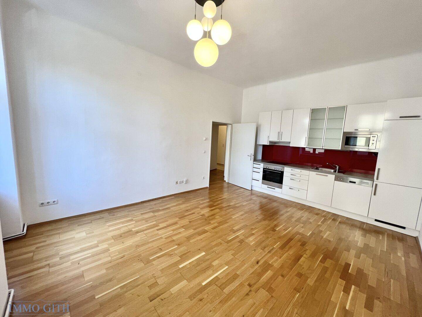 Offener Wohnbereich mit integrierter moderner Küche und Parkettboden, ideal für geselliges Beisammensein.