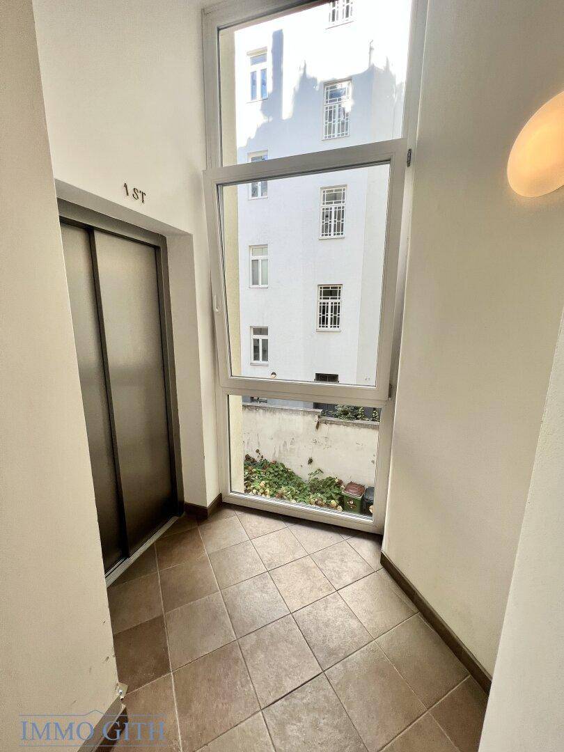 Heller Flurbereich mit Aufzugzugang und großem Fenster mit Blick auf den Innenhof.