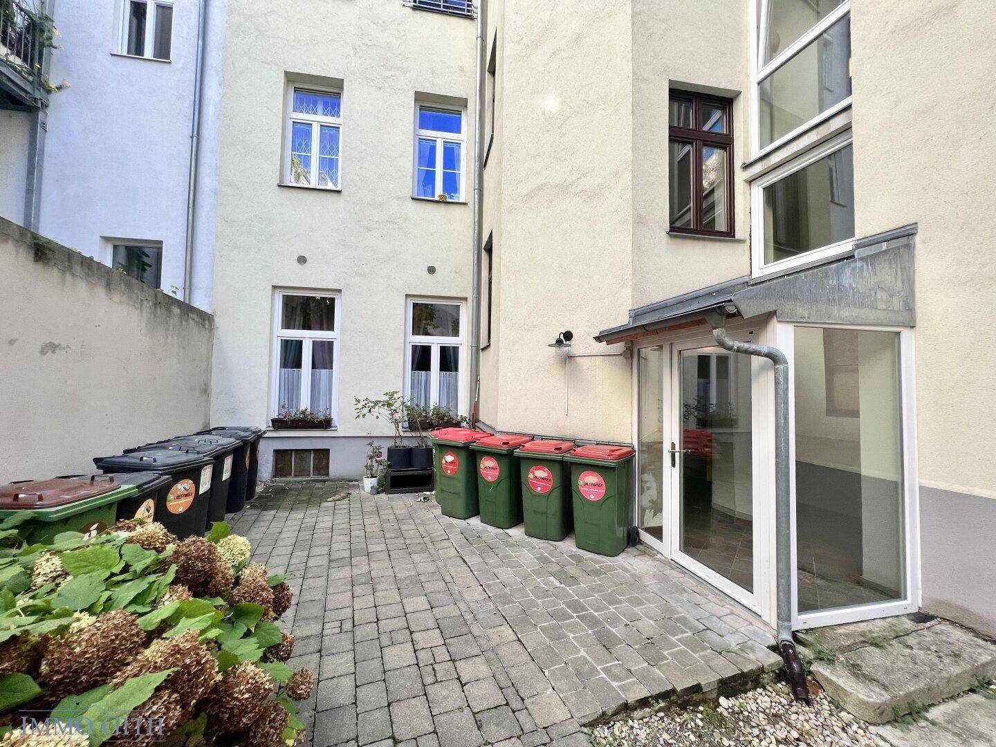 Gepflasterter Innenhof mit Mülltonnen und einem Eingangsbereich zu den Wohnungen, funktional und ordentlich.