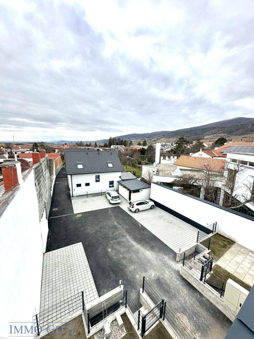 Blick von oben auf ein modernes Neubauhaus mit Parkplätzen und umliegender Landschaft.