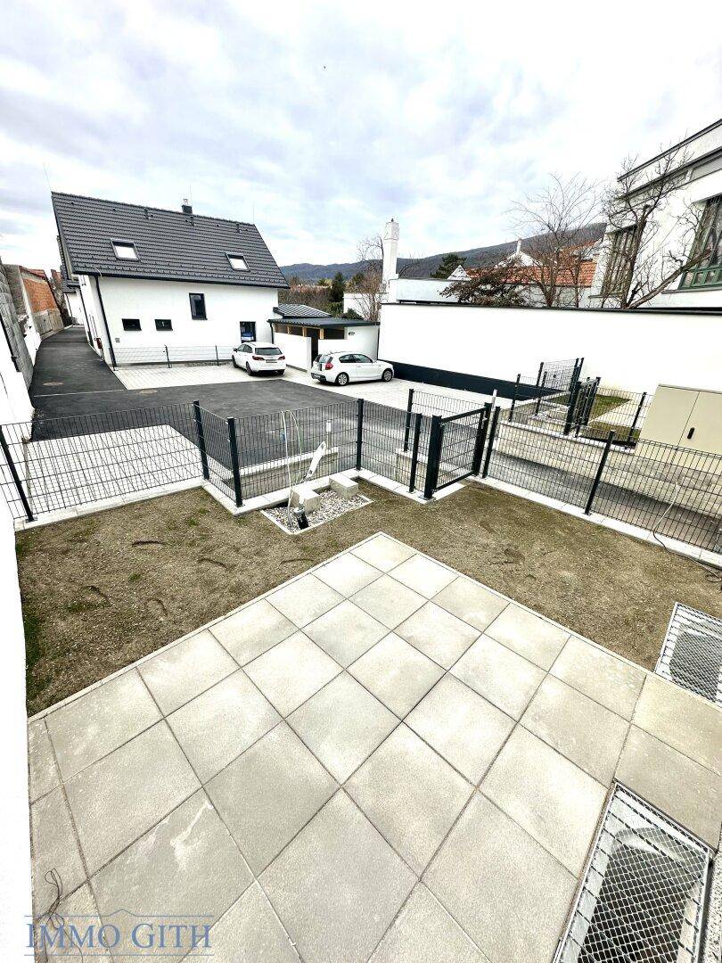 Blick auf einen kleinen Gartenbereich mit Rasen und gepflasterter Fläche, umgeben von Zäunen.