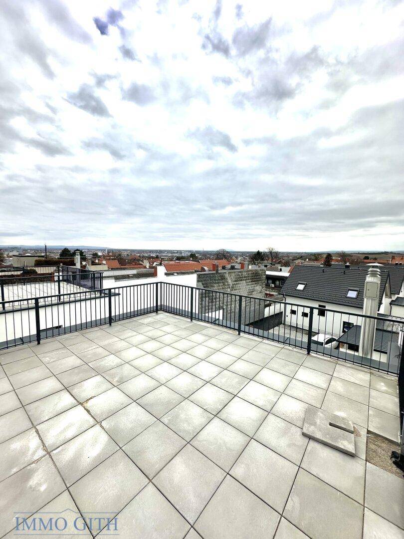 Geräumige Dachterrasse mit Fliesenboden und weitem Blick über die Dächer der Stadt und die Landschaft.