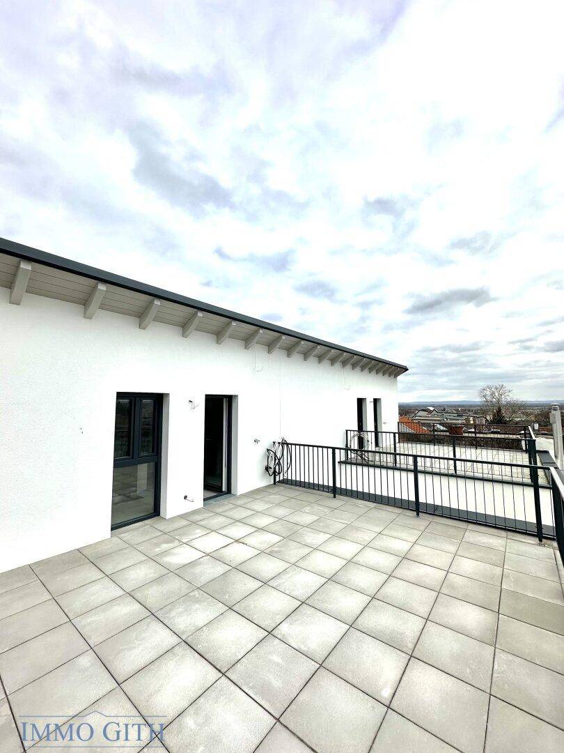 Große, geflieste Dachterrasse mit Blick auf die Umgebung und die umliegenden Gebäude unter bewölktem Himmel.