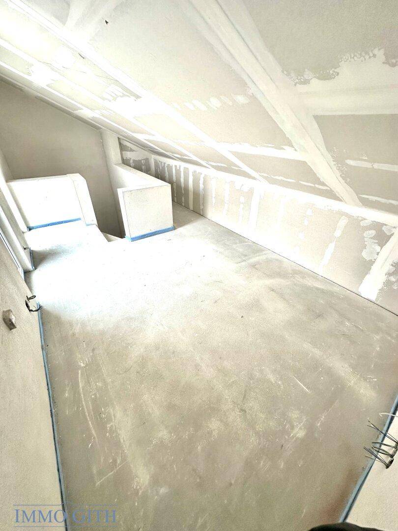 Dachgeschoss im Rohbau mit schrägen Wänden und vorbereiteten Oberflächen für den weiteren Ausbau.