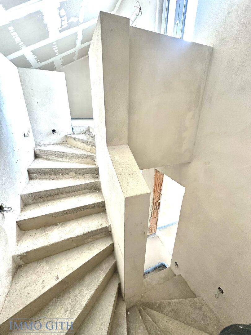 Wendeltreppe im Rohbau, die verschiedene Ebenen des Gebäudes miteinander verbindet, mit unfertigen Wänden.