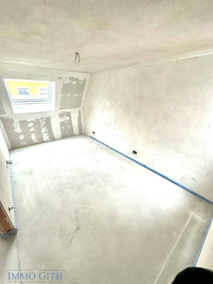 Dachgeschosszimmer im Rohbau mit Dachfenster, schrägen Wänden und viel Potenzial für den Ausbau.