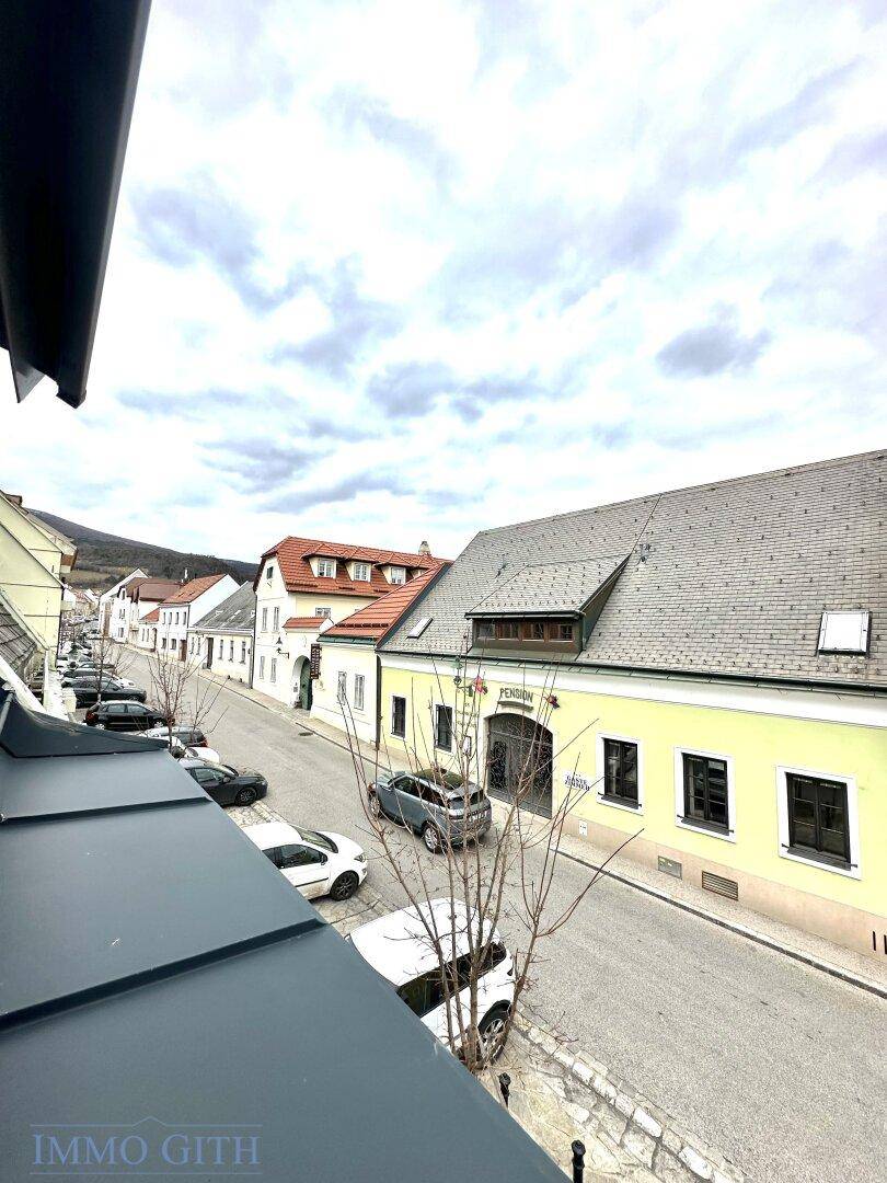 Blick von oben auf eine belebte Straße mit geparkten Autos und traditionellen Gebäuden unter bewölktem Himmel.